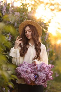Güzel bir kadın, sabah çalıların yanında bir sepet leylak çiçeği taşıyor.