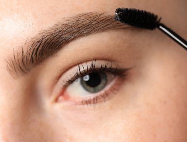 Genç bir kadın kaşlarını hortlakla fırçalıyor, yakın plan.