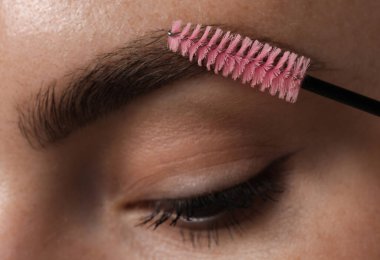 Genç bir kadın kaşlarını hortlakla fırçalıyor, yakın plan.