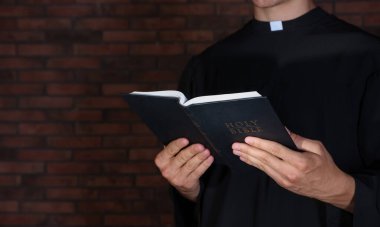 Tuğla duvarın yanında İncil 'i olan bir rahip, yakın plan. Metin için boşluk