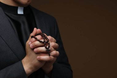 Kahverengi arka planda tespih çeken bir rahip, yakın plan. Metin için boşluk