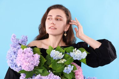 Açık mavi arka planda Hortensiya çiçekleri olan gülümseyen kadın portresi