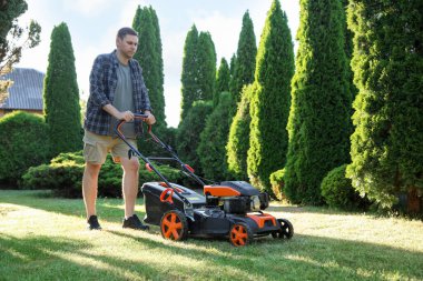 Bahçede çim biçme makinesiyle yeşil çim biçen bir adam