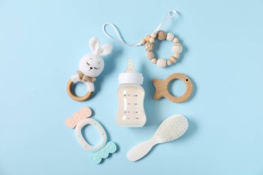 Açık mavi zemin üzerinde süt ve bebek aksesuarları olan bir şişe.