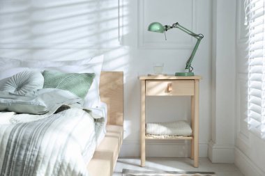 Yatak odasının yanında lamba ve bir bardak su olan komodinin yanında.