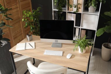 Modern bilgisayarı, kırtasiyesi ve çiçek dekoru olan şık bir iş yeri. Biyofilik iç tasarım