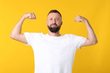 Kuvvet. Sarı arka planda pazılarını gösteren yakışıklı bir adam.