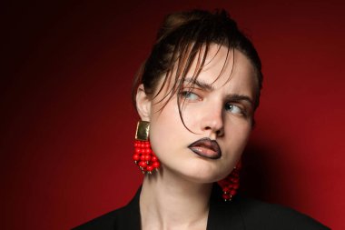Siyah dudak kalemi olan güzel bir kadın koyu kırmızı arka planda şık küpeler takıyor.