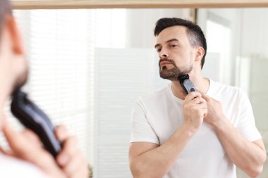 Yakışıklı adam evde aynanın yanında tıraş makinesiyle tıraş oluyor.