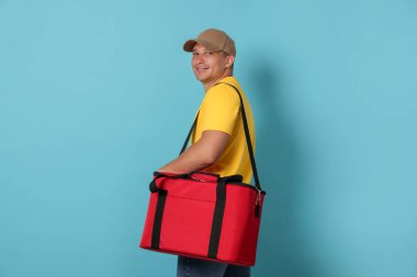 Açık mavi arka planda termo çantalı bir kurye. Yemek dağıtım servisi.