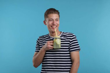 Mason kavanozundan açık mavi arka planda limonata içen gülümseyen adam. Tazeleyici içecek.