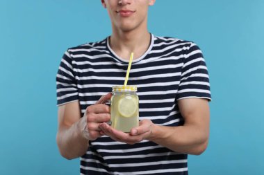 Açık mavi arka planda limonata kavanozu olan adam, yakın plan. Tazeleyici içecek.