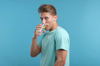 Adam açık mavi arka planda camdan ferahlatıcı bir içecek içiyor.