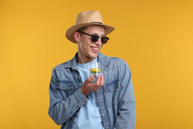 Güneş gözlüklü ve şapkalı mutlu adam sarı arka planda bir bardak ferahlatıcı içecek ile
