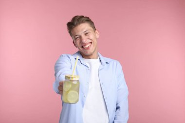 Pembe arka planda limonata kavanozu olan mutlu bir adam. Tazeleyici içecek.