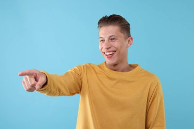 Yakışıklı adam gülüyor ve açık mavi arka plandaki bir şeye işaret ediyor. Pozitif duygu