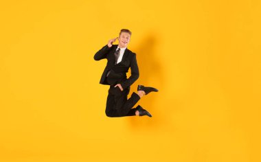 Turuncu arka planda akıllı telefondan konuşan işadamı zıplıyor