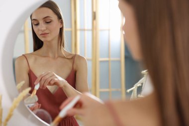 Hazırlanıyor. Kapalı mekanda aynanın yanında makyaj yapan genç bir kadın.