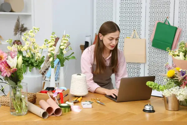 Dükkandaki tahta masada dizüstü bilgisayarla çalışan profesyonel bir çiçekçi.
