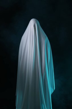 Ürkütücü hayalet. Siyah arka planda beyaz bir çarşafla kaplanmış bir adam.
