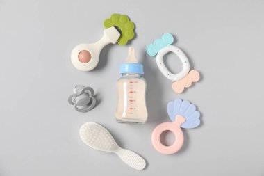 Açık gri zemin üzerinde süt ve bebek aksesuarları olan bir şişe.
