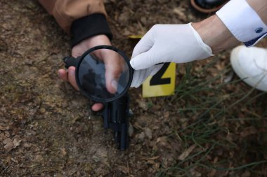 Adli tıp uzmanlığı. Olay yerinde büyüteçle çalışan dedektif dışarıda ölü bir adamın cesediyle birlikte çalışıyor.