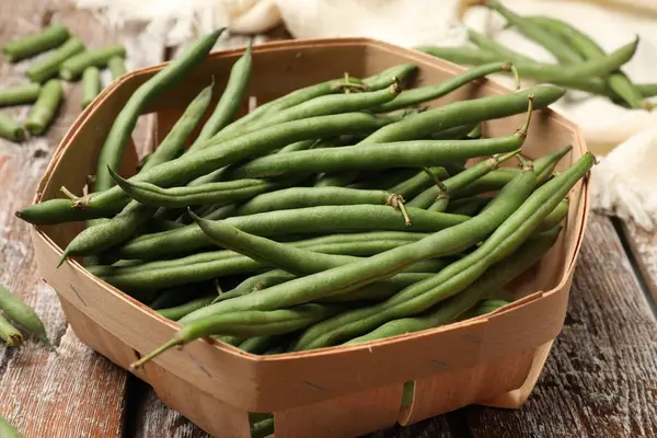 Taze bezelye kabukları sepetin içinde renkli ahşap masa üzerinde, yakın plan.