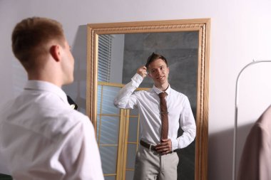 Yakışıklı bir adam aynanın yanında saçını tarıyor.