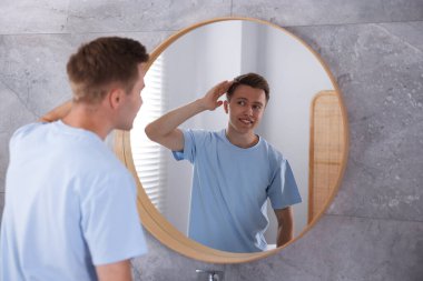 Genç adam evde aynanın yanında hazırlanıyor.