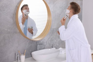 Hazırlanıyor. Genç adam evde aynanın yanında kremayla tıraş oluyor.