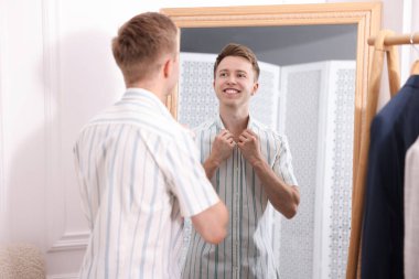 Hazırlanıyor. Genç adam aynanın yanında kıyafet deniyor.