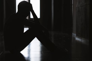 Üzüntü ve depresyon. Karanlık odada yerde oturan bir adamın silueti.