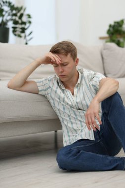 Üzgün düşünceli adam evdeki kanepeye yaslanıyor.