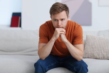 Evdeki kanepede üzgün, düşünceli bir adam.