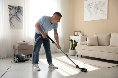 Evin zeminini elektrikli süpürgeyle temizleyen adam.