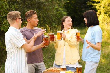 Bir grup mutlu arkadaş dışarıda bira bardaklarını tokuşturuyor.