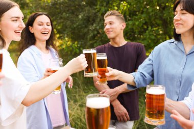 Bir grup mutlu arkadaş dışarıda bira bardaklarını tokuşturuyor.