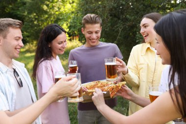 Pizza yiyip dışarıda bira içen bir grup mutlu arkadaş.