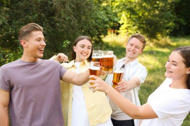 Bir grup mutlu arkadaş dışarıda bira bardaklarını tokuşturuyor.