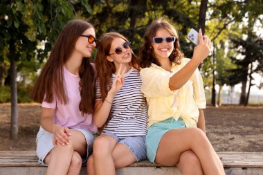 Güneş gözlüklü mutlu arkadaşlar bankta selfie çekiyorlar.