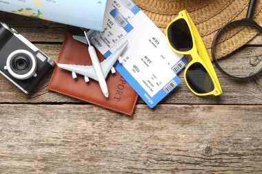 Yaz tatili zamanı. Dünya haritası, pasaport, uçuş biletleri, oyuncak uçak, kamera, büyüteç ve plaj aksesuarları ahşap masada, düz yerde. Metin için boşluk
