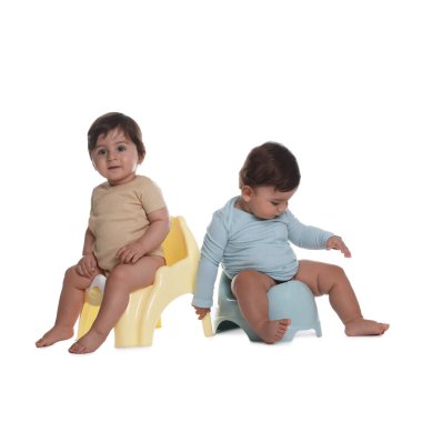 Beyaz arka planda lazımlıkların üzerinde oturan sevimli küçük bebekler.