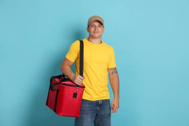 Açık mavi arka planda termo çantalı bir kurye. Yemek dağıtım servisi.