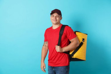 Açık mavi arka planda termo çantalı bir kurye. Yemek dağıtım servisi.