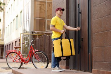 Dışarıdaki binanın yakınında termo çantalı bir kurye. Yemek dağıtım servisi.