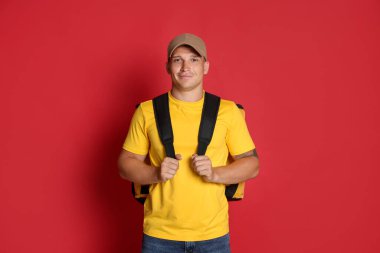 Kırmızı arka planda termo çantalı bir kurye. Yemek dağıtım servisi.