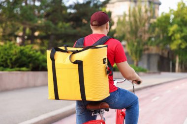 Termo çantalı bir kurye dışarıda bisiklet sürüyor, arkadan bakıyor. Yemek dağıtım servisi.