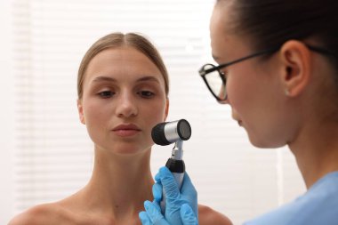 Doktor hastanede dermatoskopla genç kadının benini inceliyor.