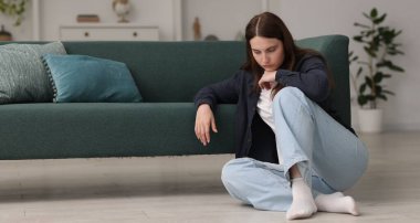 Üzgün genç kadın evde yerde oturuyor, mesaj için yer var.