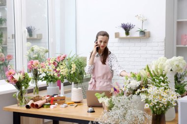 Profesyonel çiçekçi dükkanda çalışırken akıllı telefondan konuşuyor.